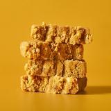 stack of two halved lemon coconut protein bar pieces against a vibrant yellow background.