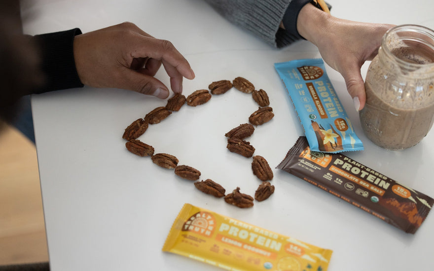 a heart made out of pecans on a white table surrounded by healthy truth protein bars