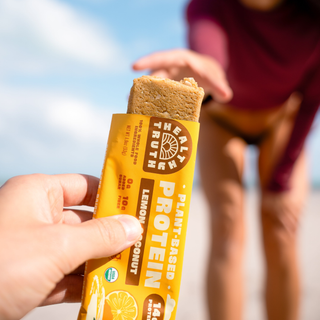 A woman in a swim suit reaching for a lemon protein bar being held by a hand 