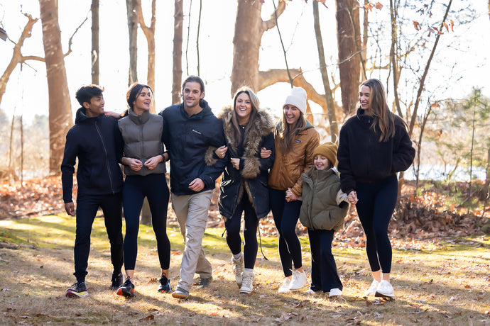 Group photo of 7 friends walking through the woods white holding hands and smiling